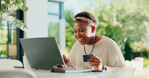 An African American woman using her credit card to make a purchase on her laptop.